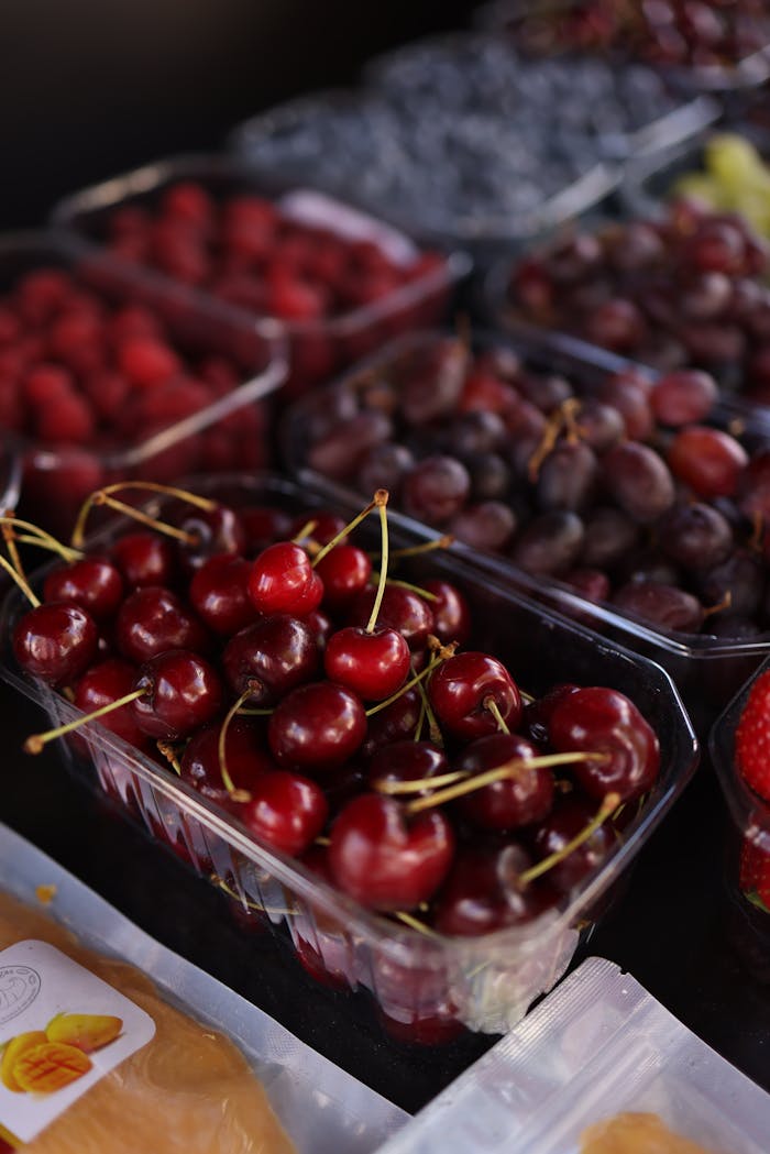 A mouthwatering display of fresh cherries and various berries in plastic containers at a market stall.