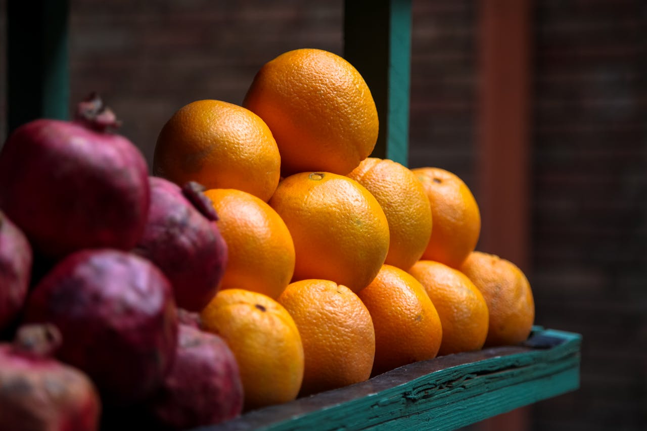 A vibrant display of fresh ripe oranges and pomegranates at an outdoor market stall.